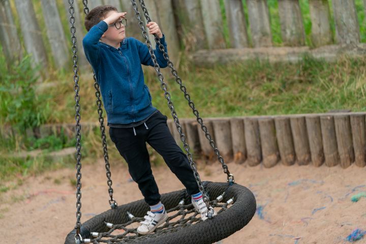 child playing on swing whilst peering with hand to forehead